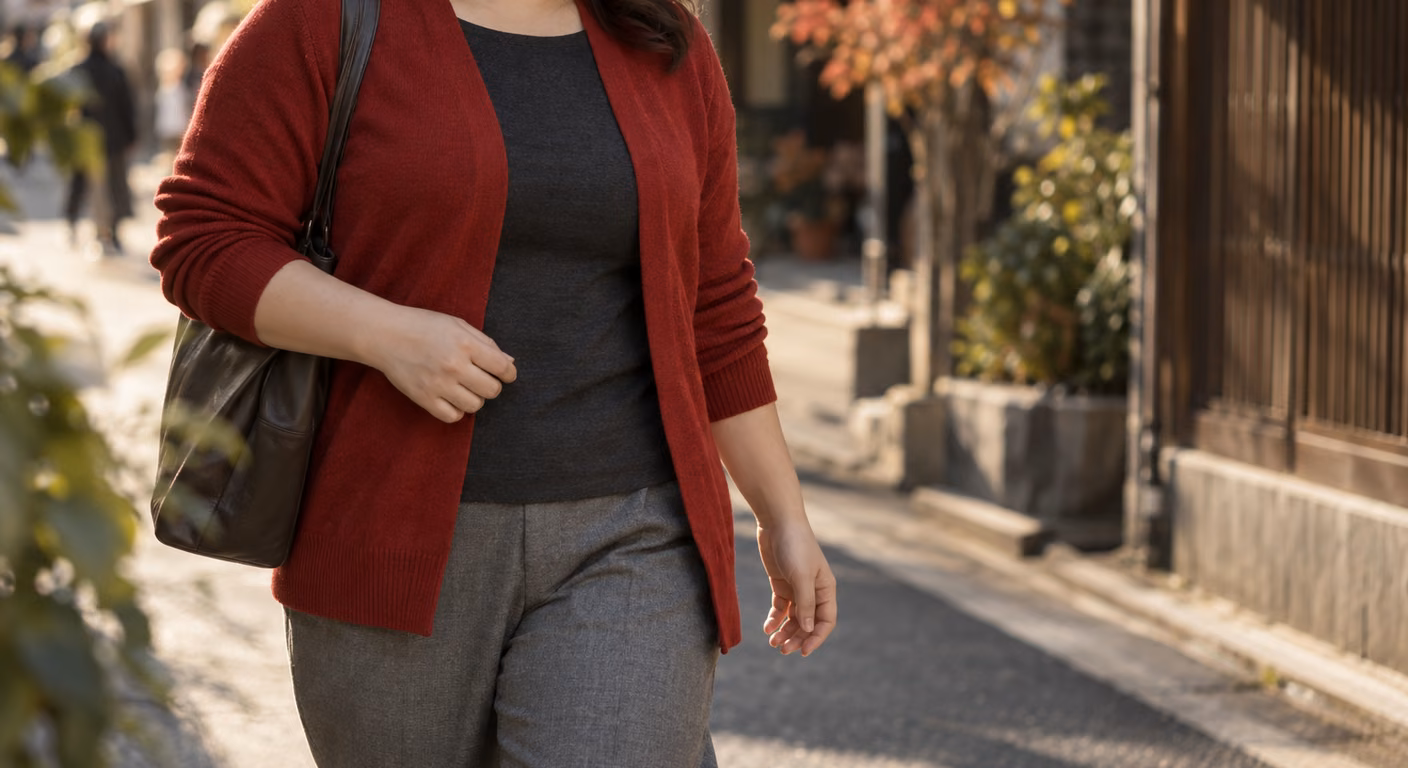 前を開けた赤いカーディガンの間から暗い色のトップスが縦にのぞく、ふくよかな体型の女性の胸元から膝までの秋の装い