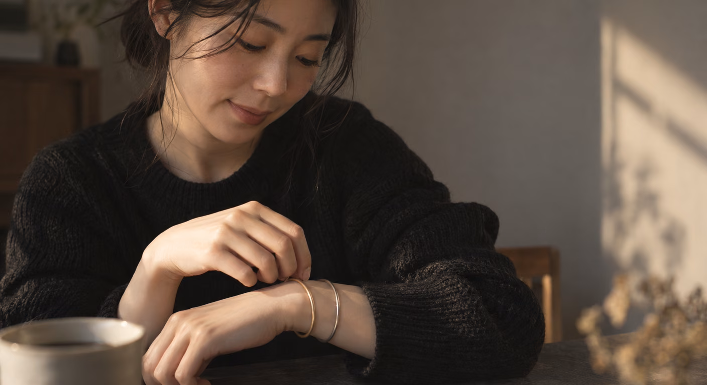 黒いニットの袖口からのぞく手首で、白っぽい淡い金のつや消しの腕輪と細い銀の腕輪を指で回している手元
