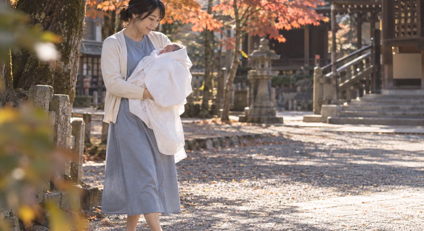 紅葉の始まった神社の境内で、くすんだ水色のワンピースに生成りのカーディガンを羽織った女性が、白いおくるみの赤ちゃんを抱いて歩いている