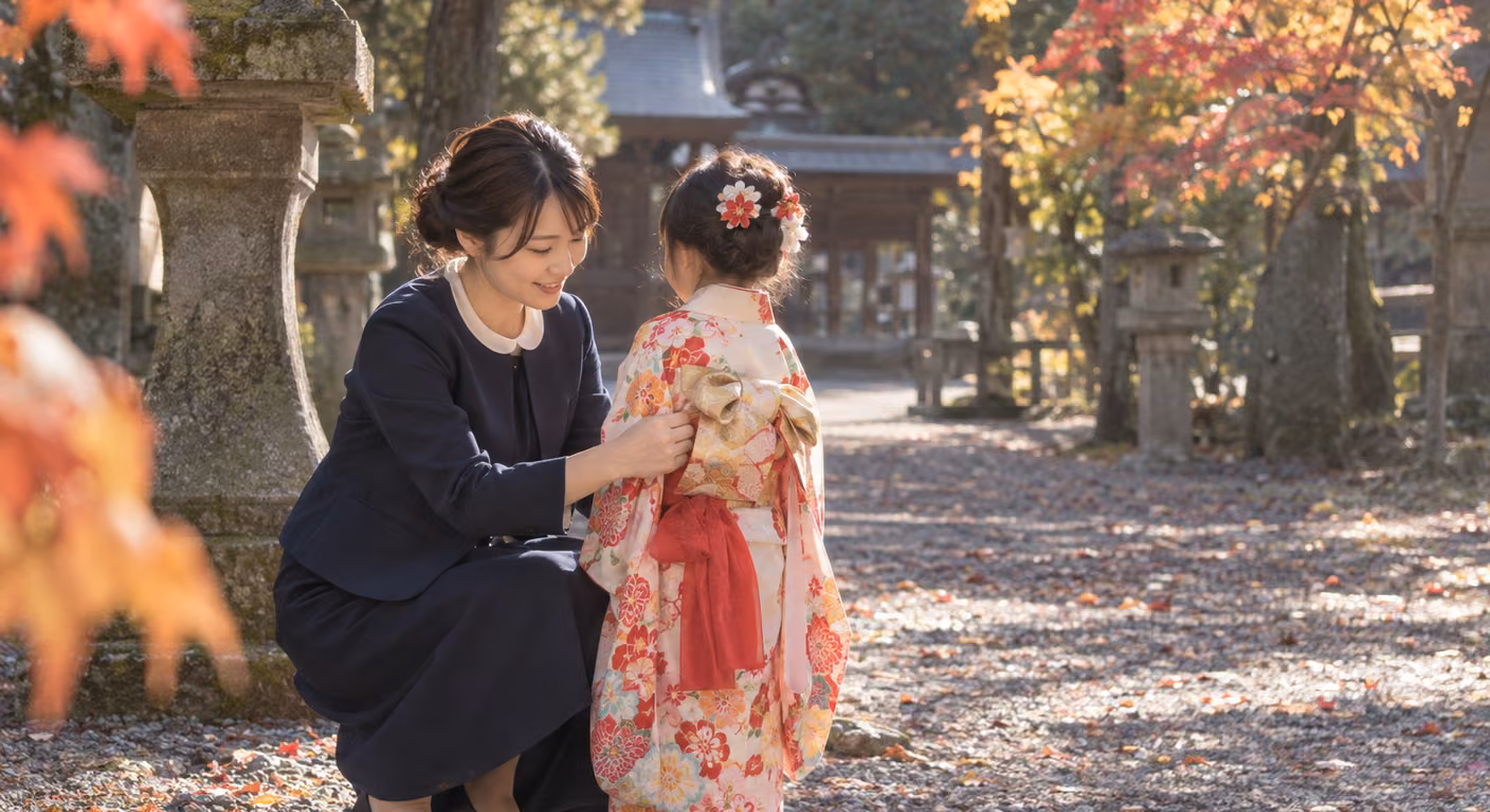 紅葉の色づいた神社の参道で、紺のジャケットの襟元から白い小さな丸襟をのぞかせた母親が、着物姿の子の帯を直すためにしゃがんでいる