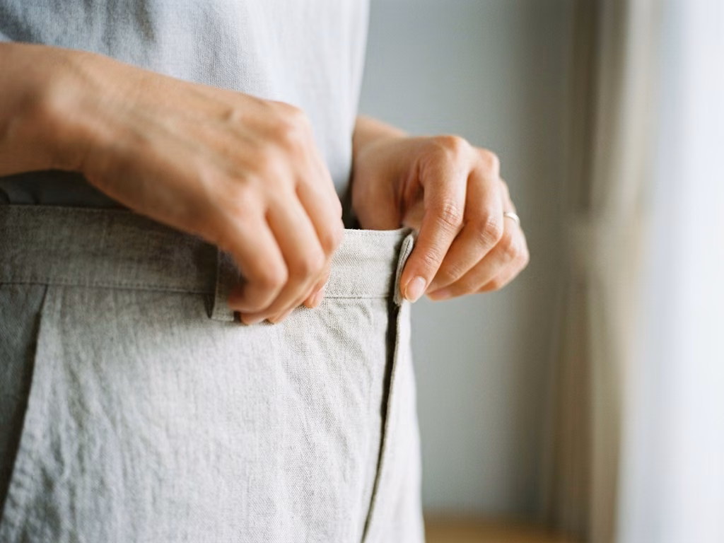 腰の位置で布の端をつまんで、布が終わる高さを指で確かめているところ